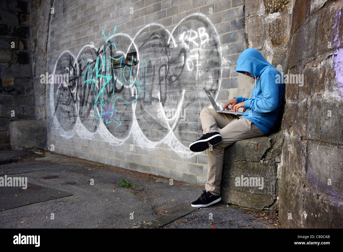 En informatique, hacker, siège de conspirateur avec un ordinateur portable, en face d'un graffiti. Photo symbole, de la criminalité sur Internet. Banque D'Images