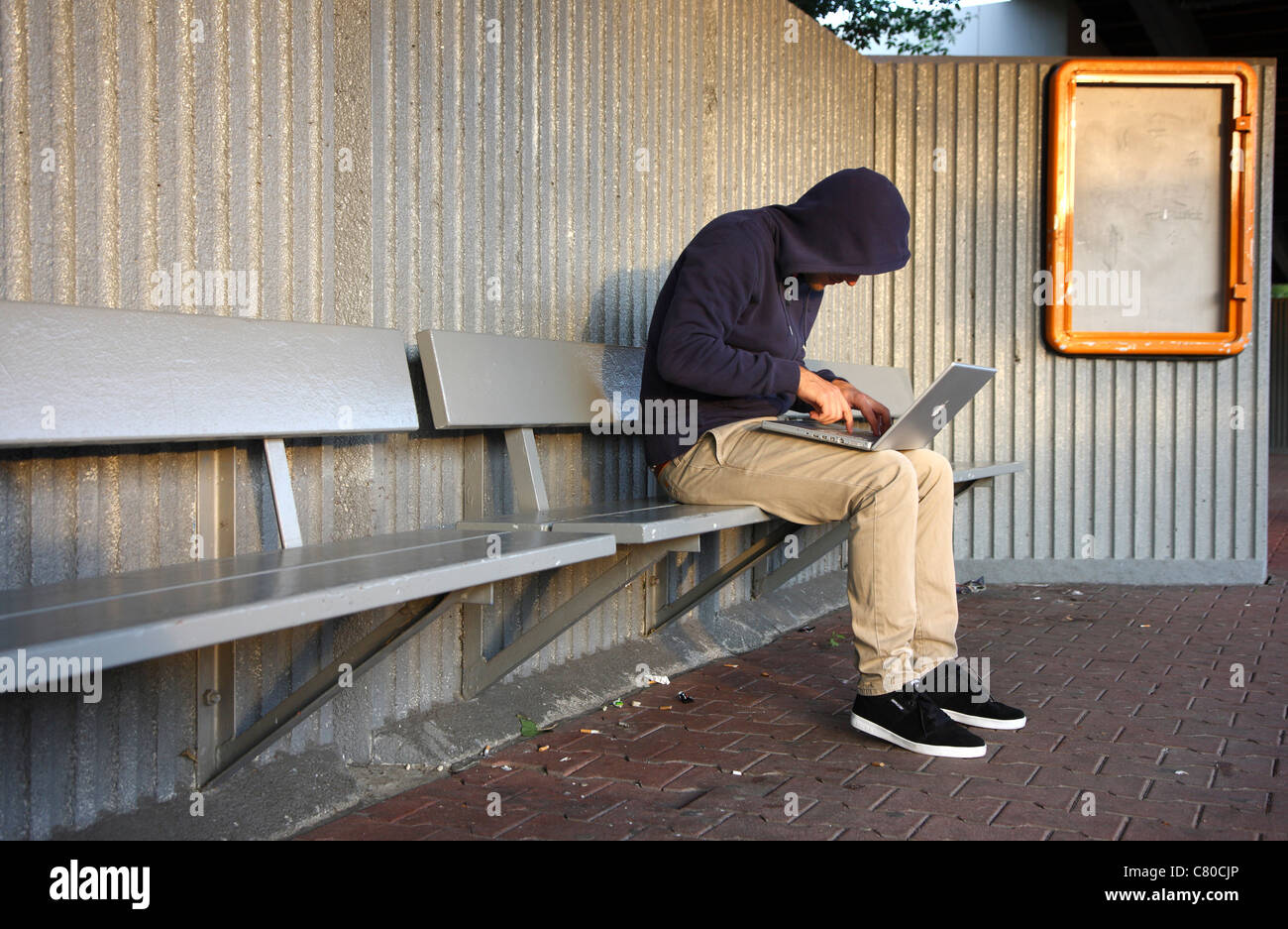 En informatique, hacker, siège de conspirateur, à l'extérieur, dans un abri-bus, avec un ordinateur portable. Photo symbole, de la criminalité sur Internet. Banque D'Images