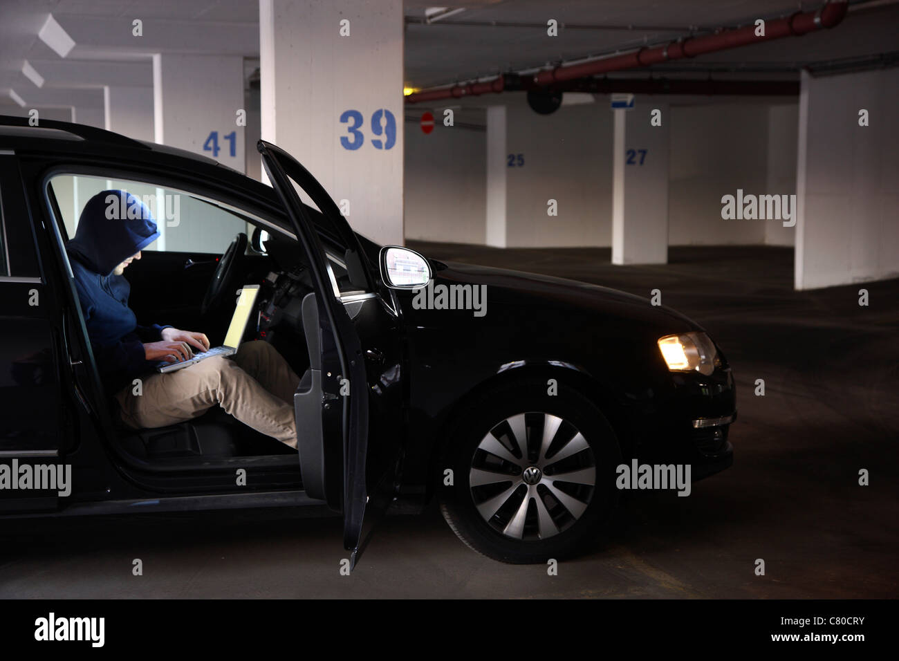 En informatique, hacker, siège de conspirateur, dans un parking couvert, avec un ordinateur portable. Photo symbole, de la criminalité sur Internet. Banque D'Images