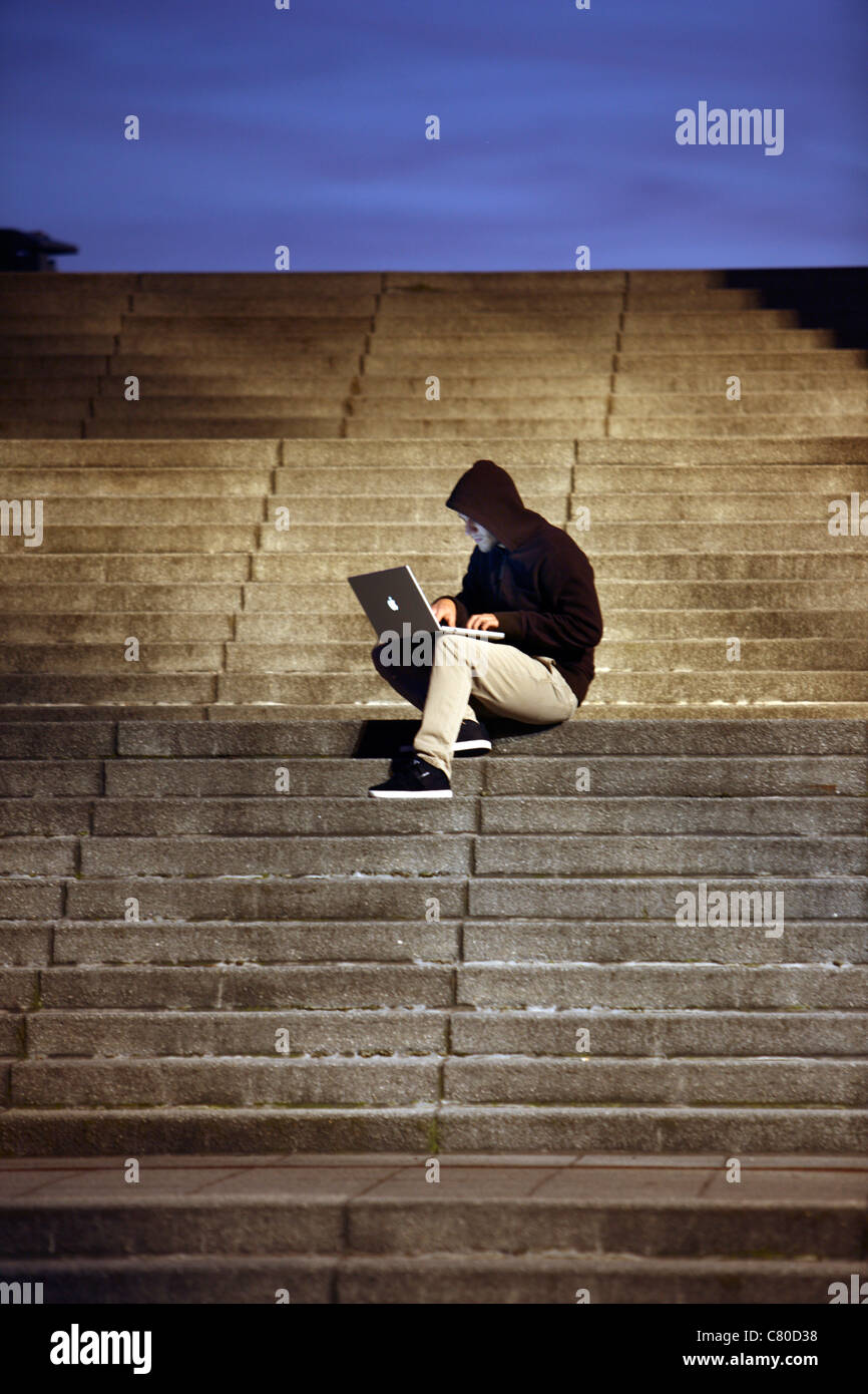 En informatique, hacker, siège de conspirateur, à l'extérieur, sur les escaliers, avec un ordinateur portable. Photo symbole, de la criminalité sur Internet. Banque D'Images