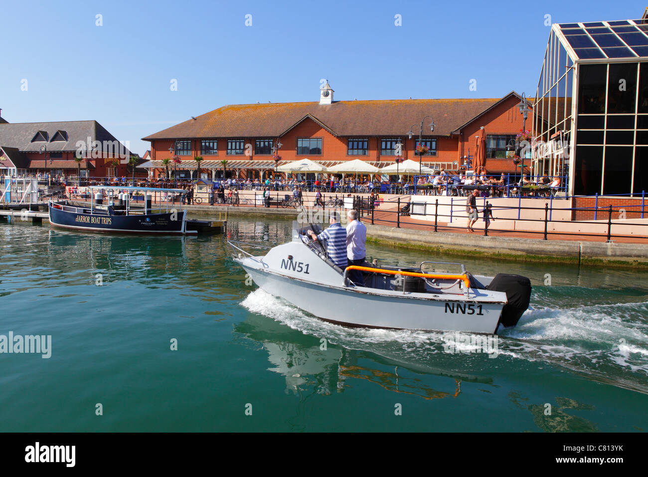 Bateau passant devant les cafés du bord de mer de Lower Quayside, Sovereign Harbour, Eastbourne, East Sussex, Angleterre GB Banque D'Images
