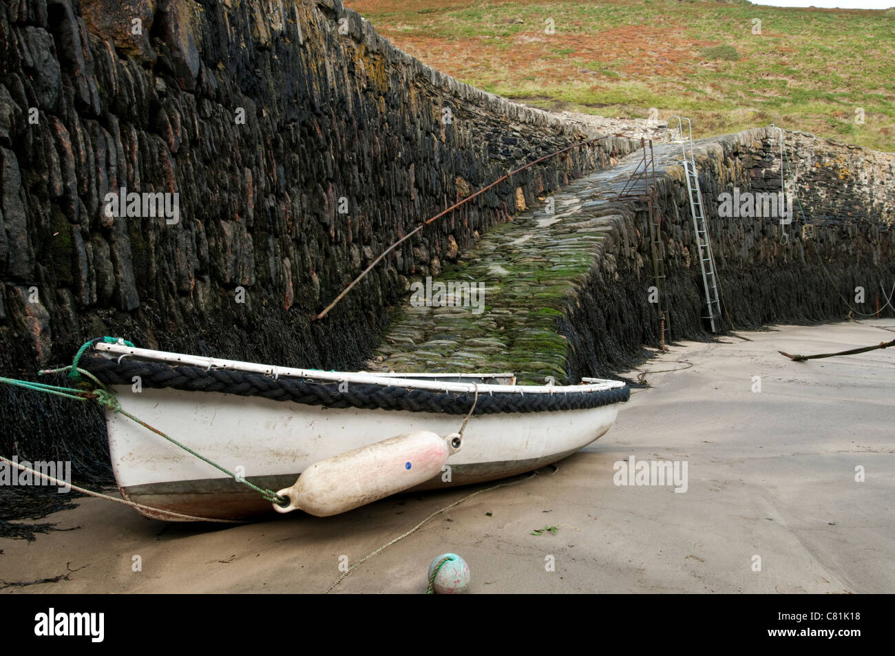 Un petit bateau amarré au mur du port à marée basse. Banque D'Images