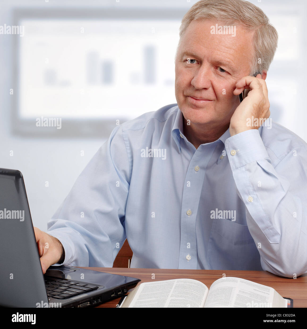 Man talking on phone and smiling in avant de l'ordinateur et la Bible Banque D'Images