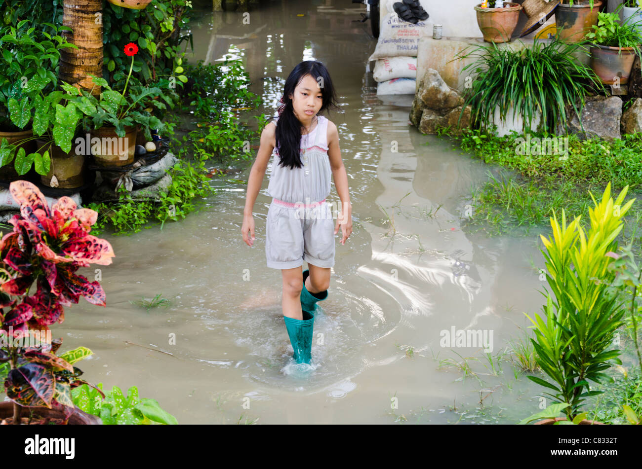 Une jolie fille asiatique de 9 ans avec de longs cheveux noirs porter des bottes de promenades à travers l'eau jusqu'aux chevilles dans une cour inondée en Thaïlande Banque D'Images