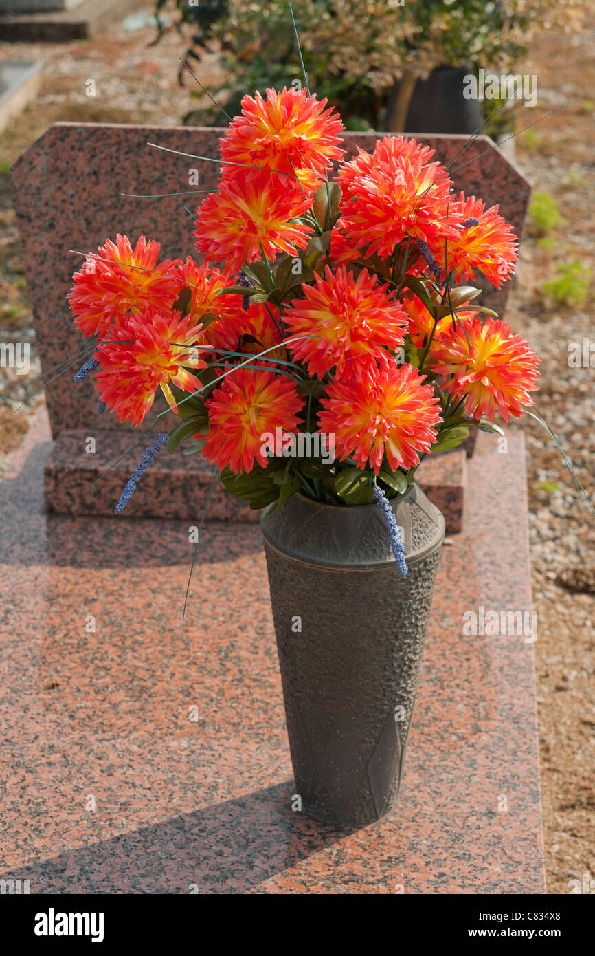 Pierre tombale dans un cimetière décoré de fleurs artificielles Banque D'Images