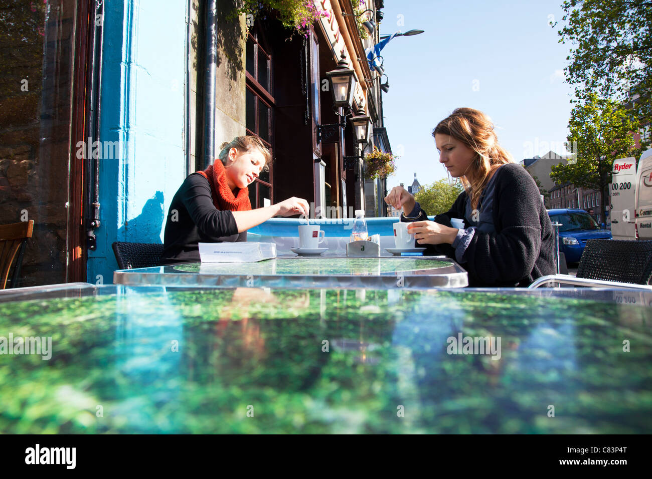 Deux jeunes filles ayant un café dans grassmarket Édimbourg en remuant à discuter et boire à l'extérieur en plein air table Banque D'Images