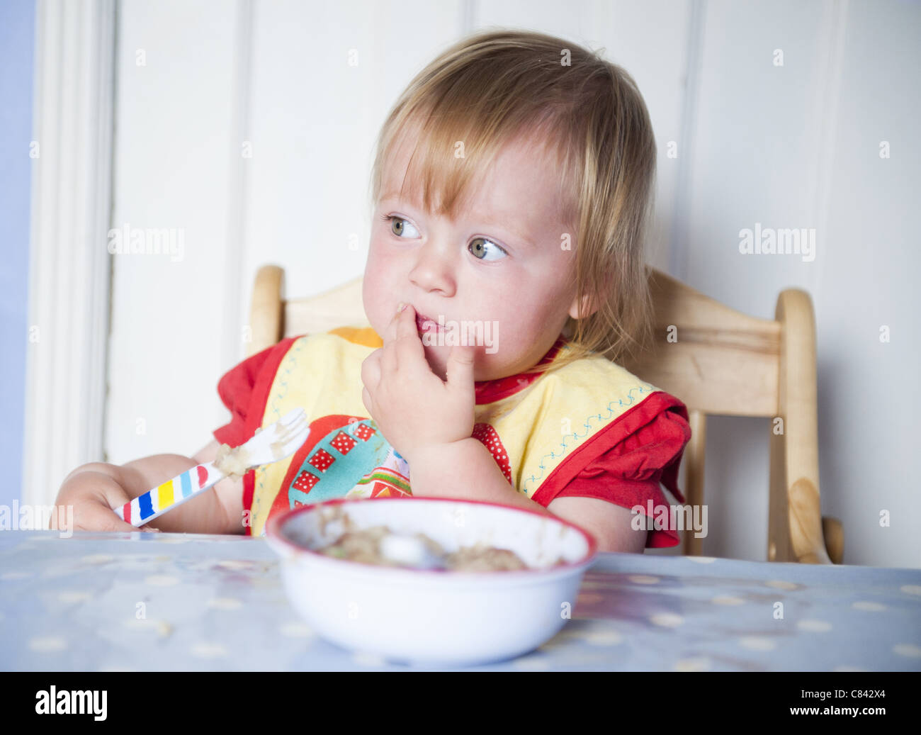 Bébé fille bavoir en mangeant à table Banque D'Images