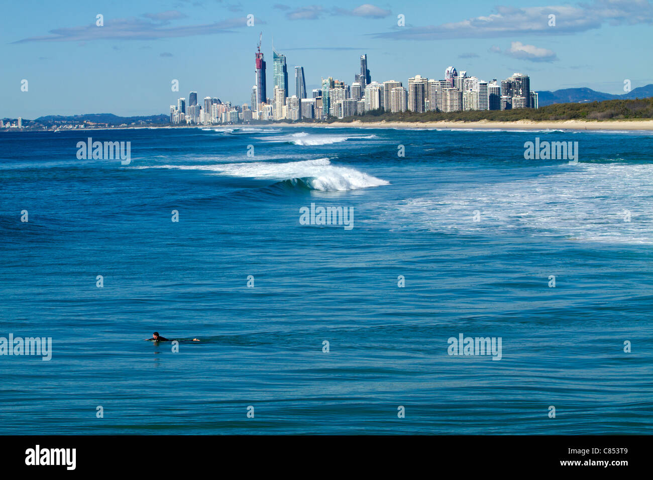 Un surfeur pagayer vers une vague avec Surfers Paradise dans l'arrière-plan. Banque D'Images