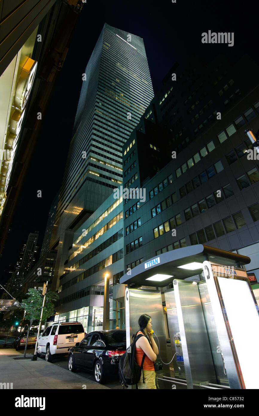 Jeune fille avec un sac à dos de parler sur un téléphone public tard dans la soirée du 53e st à New York City Banque D'Images