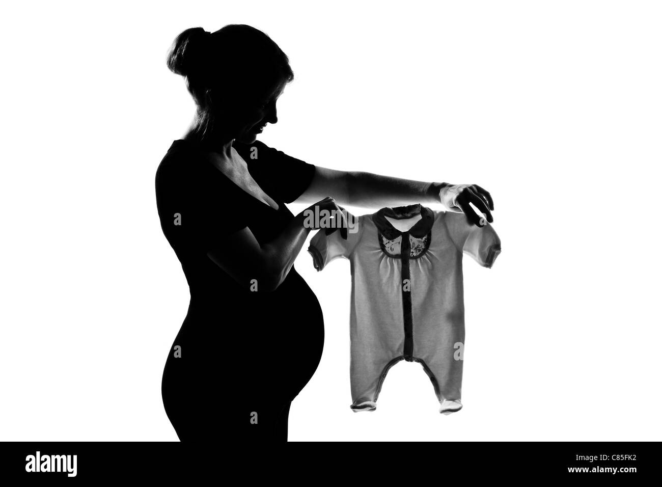 Une belle caucasian pregnant woman holding vêtements de bébé en silhouette sur fond blanc isolé studio Banque D'Images