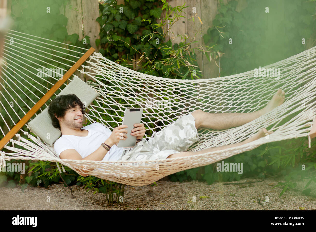 Mixed Race man laying in hammock using digital tablet Banque D'Images