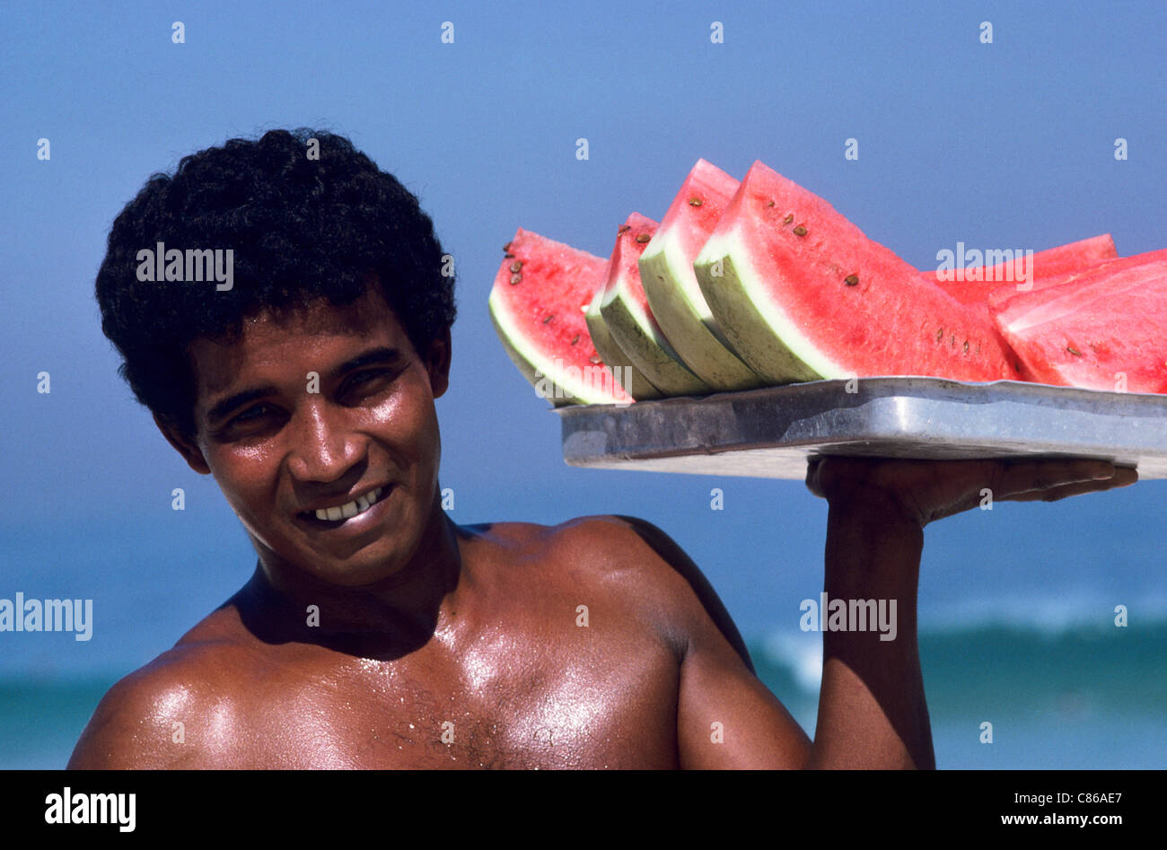 Rio de Janeiro, Brésil. Jeune homme portant un plateau de succulentes tranches de melon d'eau à vendre sur la plage. Banque D'Images