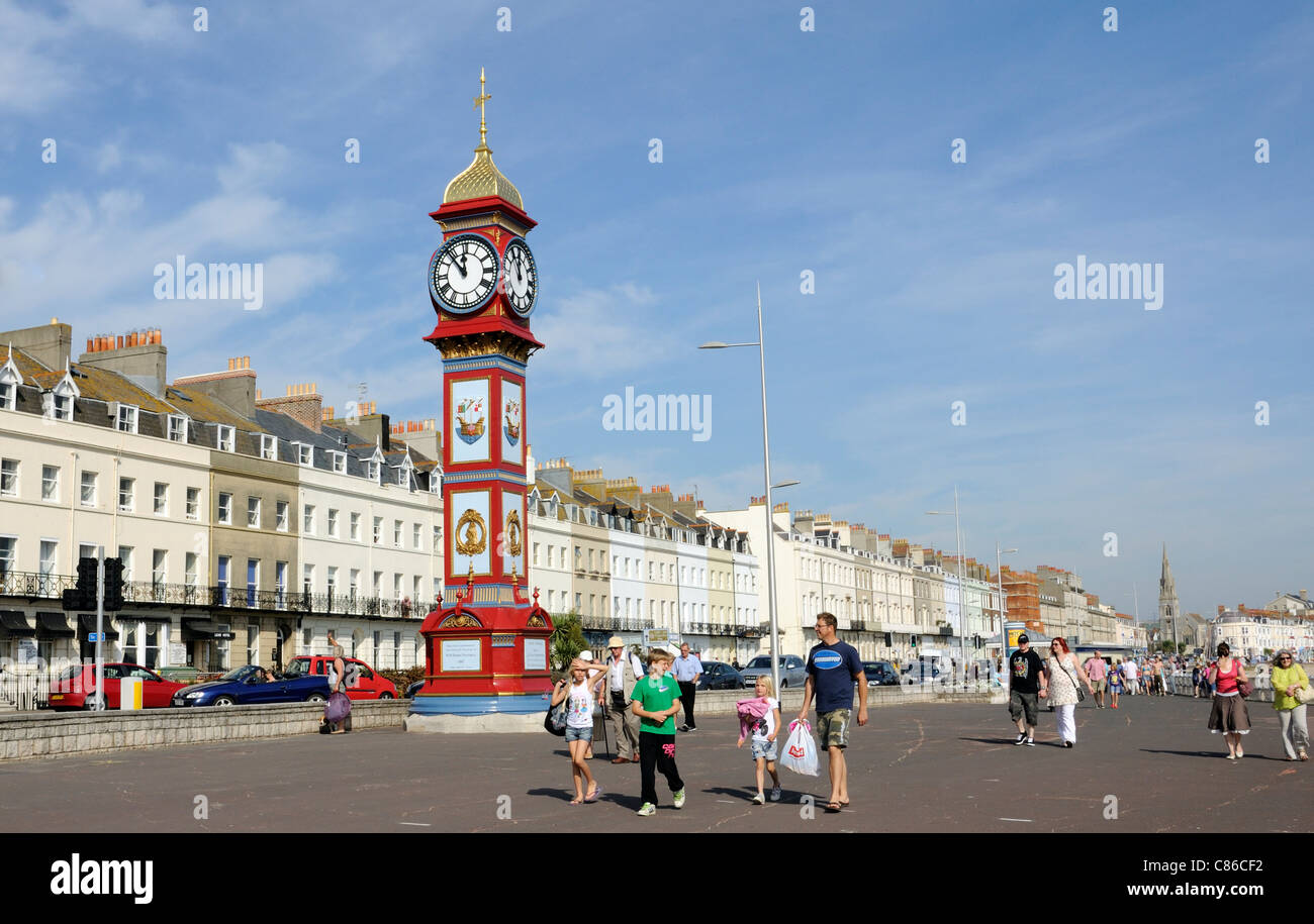 Les vacanciers sur la promenade Weymouth Dorset England UK La tour de l'horloge érigée pour célébrer le jubilé de la reine Victoria Banque D'Images