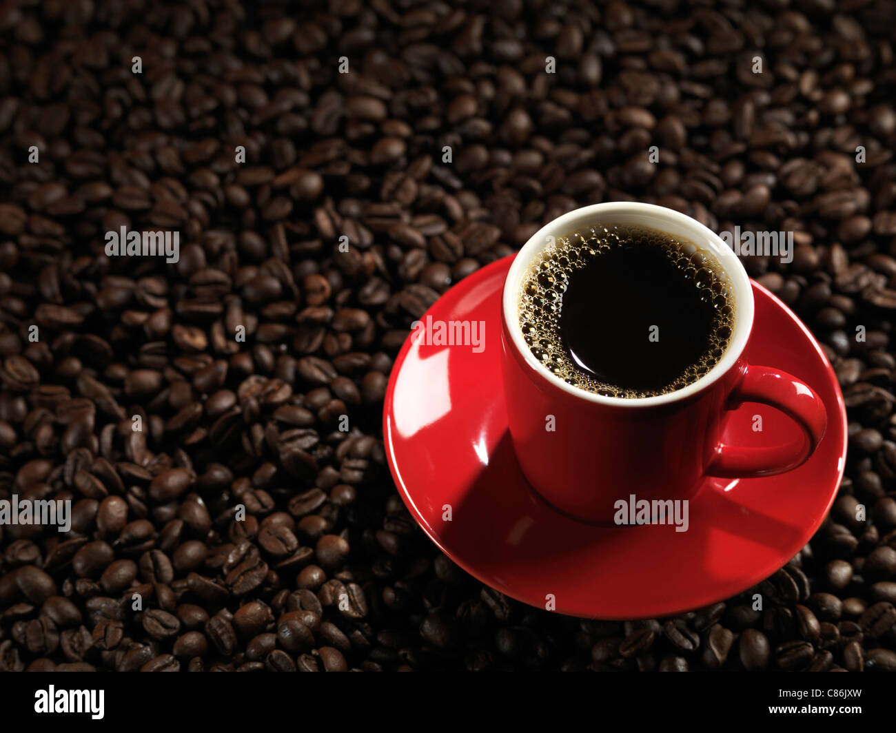 Tasse de café rouge avec une soucoupe sur fond de grain de café Banque D'Images