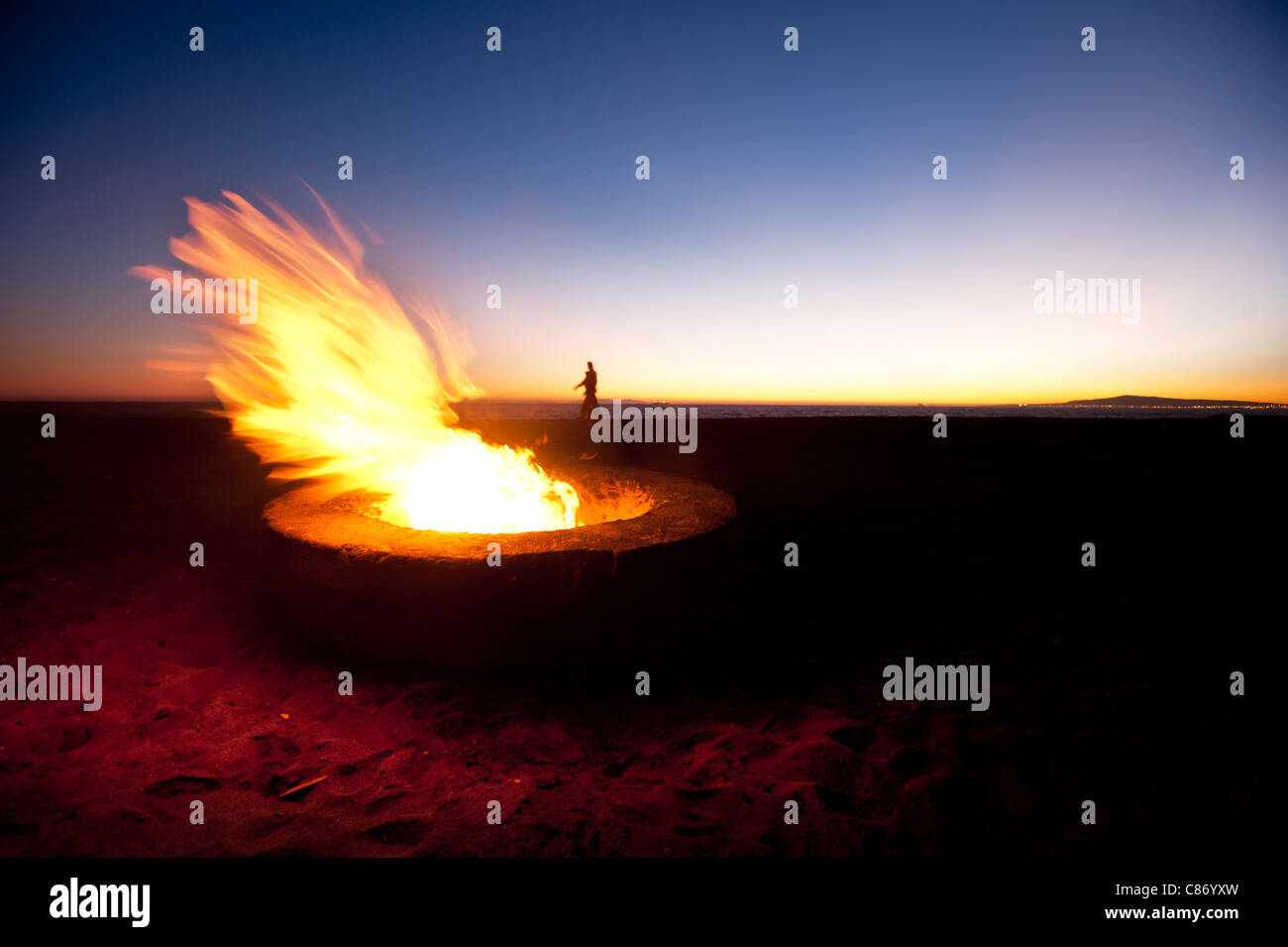 Quelques promenades le long d'une plage derrière un grand feu au coucher du soleil. Banque D'Images