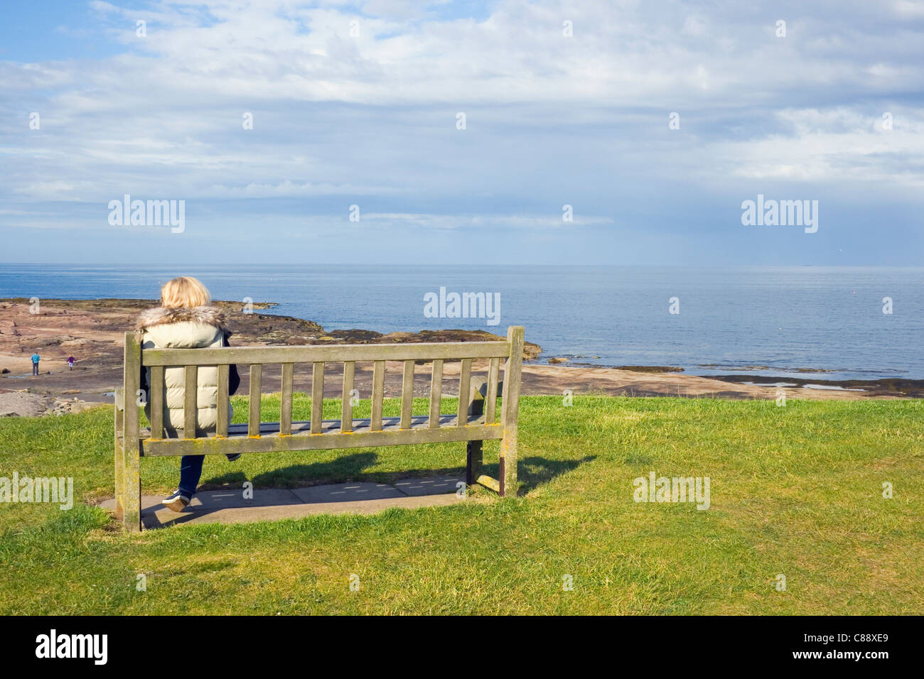 Femme solitaire assis sur un banc avec vue sur la plage. Largs, côte de Northumberland, en Angleterre. Banque D'Images