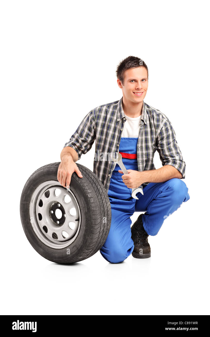 Un mécanicien homme posant avec un pneu de rechange et la tenue d'une clé Banque D'Images