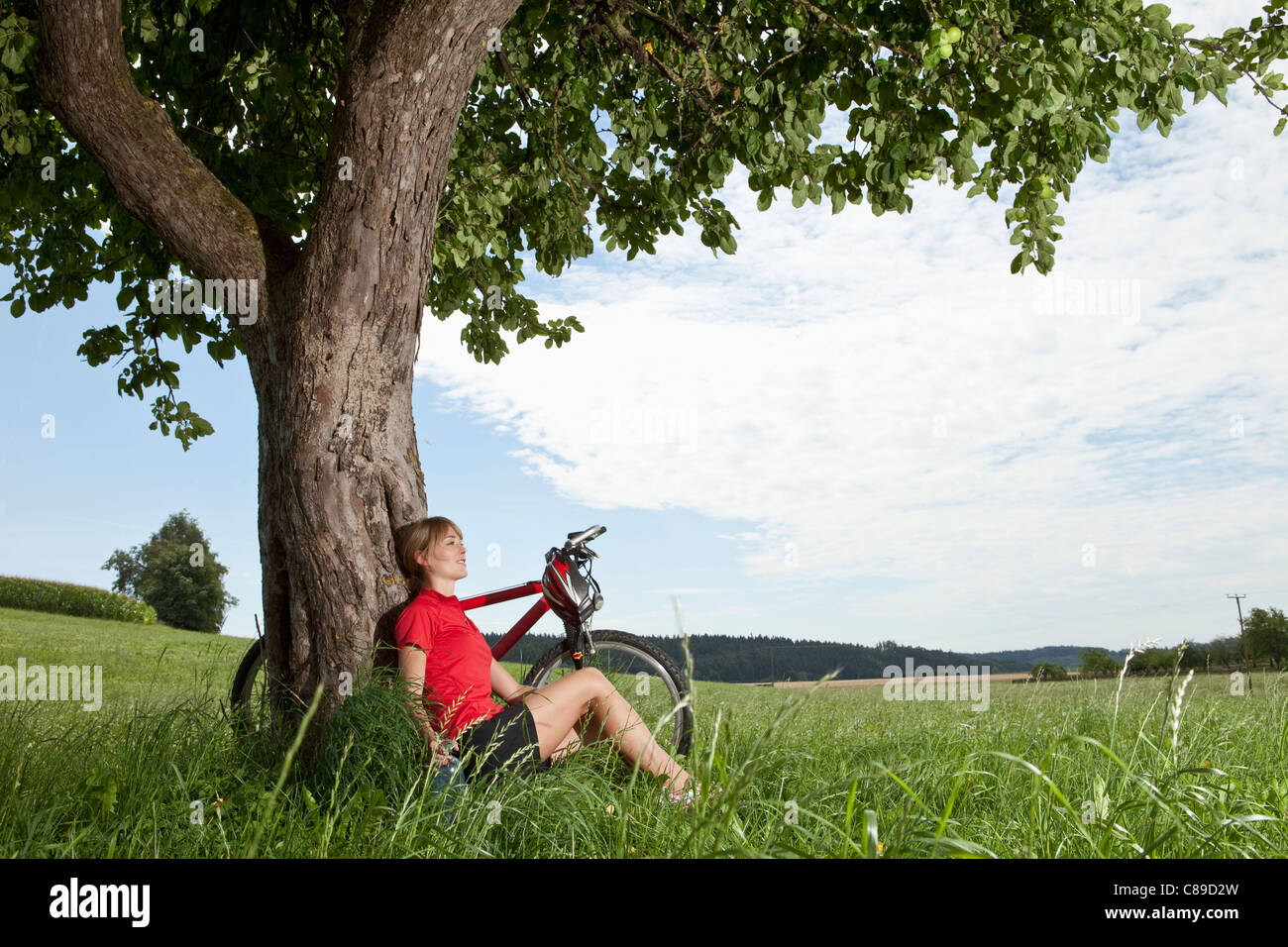 Allemagne, Bavière, jeune femme assise contre l'arbre avec vtt Banque D'Images