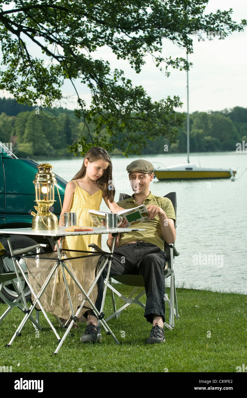 Allemagne, Bavière, Woerthsee, père et fille livre lecture près de lac en camping Banque D'Images