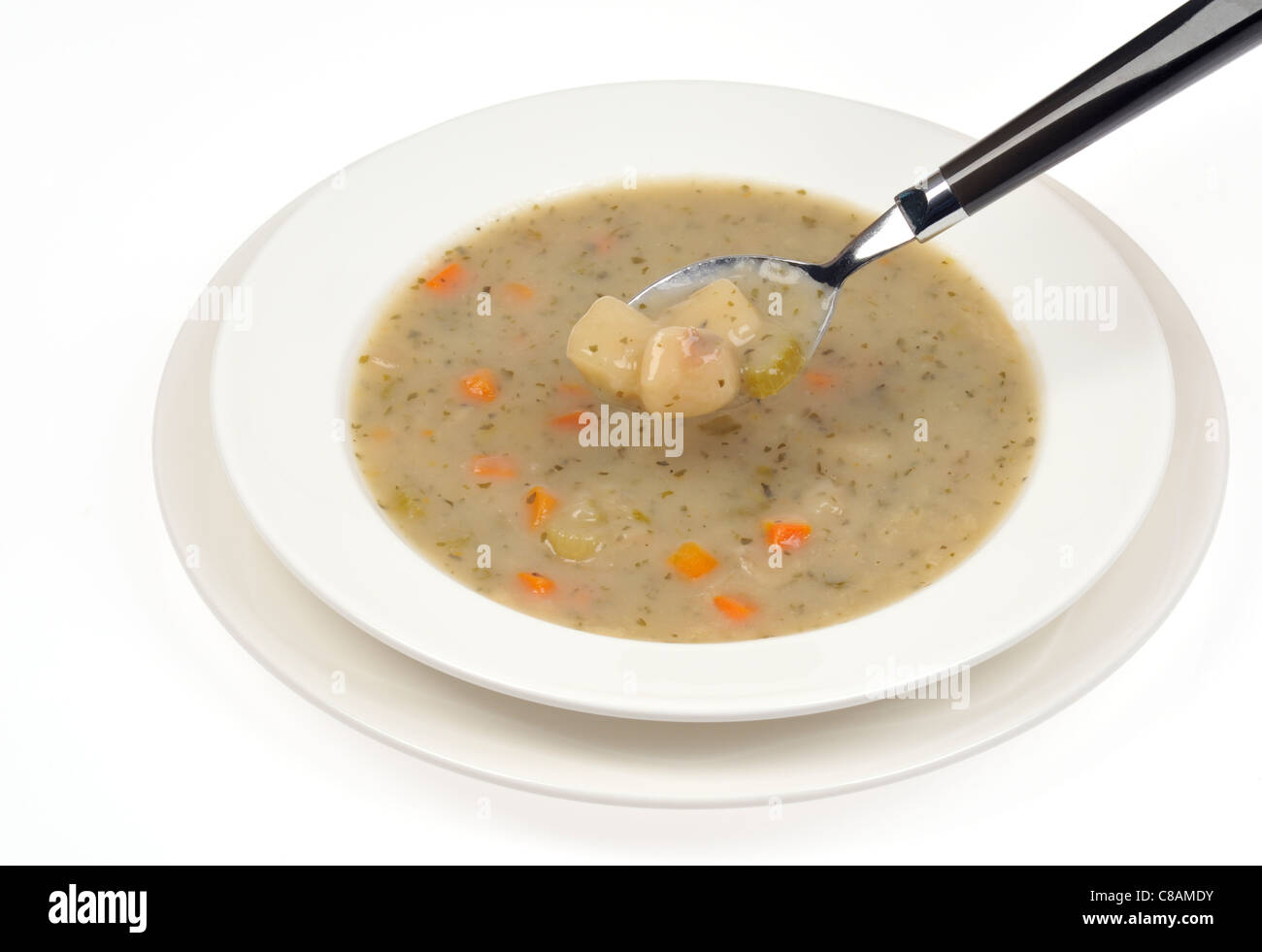 Un bol de soupe aux poireaux et pommes de terre avec cuillerée à soupe sur fond blanc. Banque D'Images