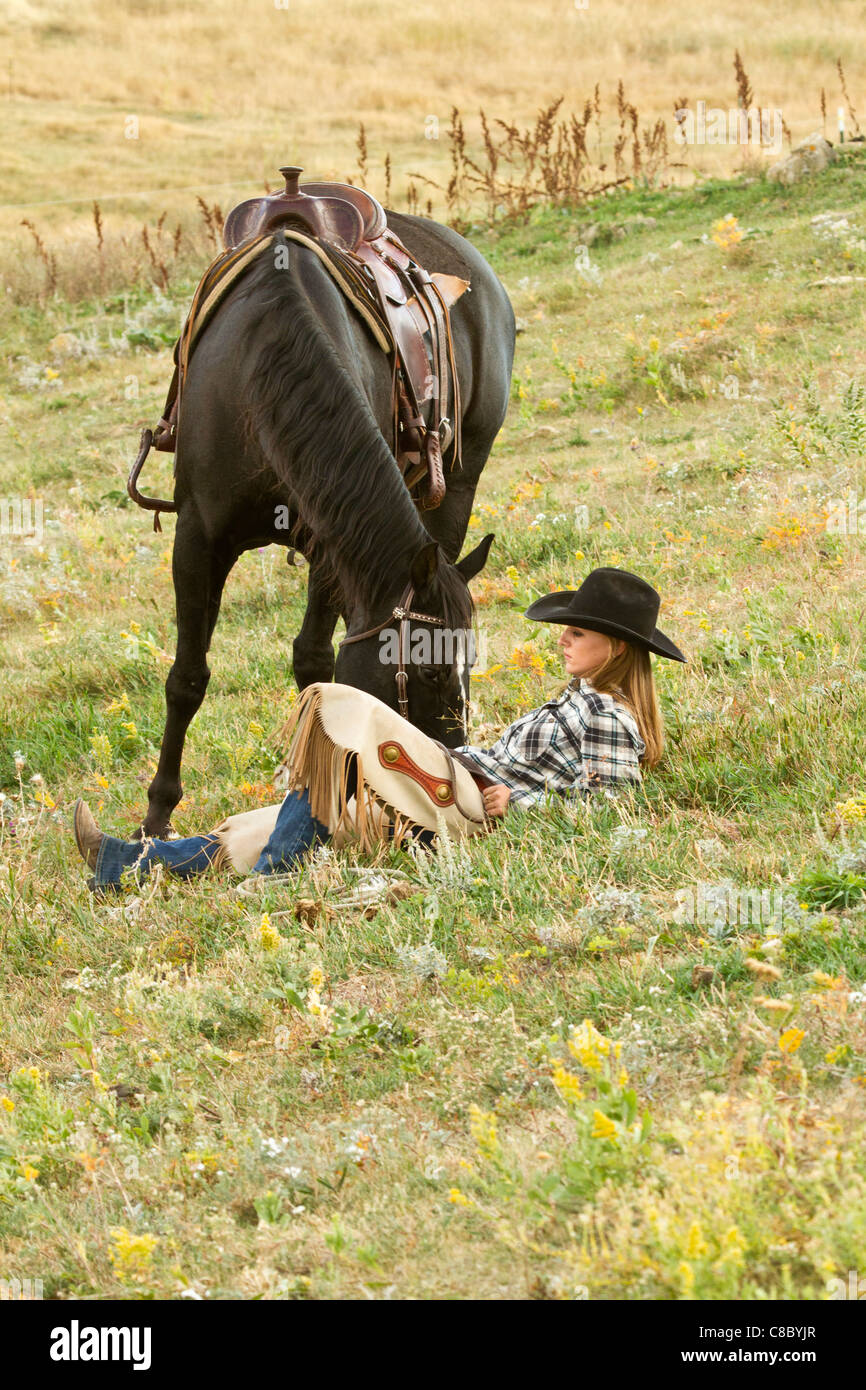 Cowgirl reposant parmi les fleurs sauvages dans un champ à côté de son cheval Banque D'Images