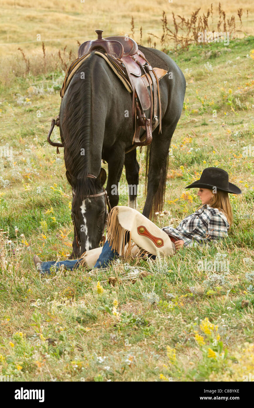 Cowgirl reposant parmi les fleurs sauvages dans un champ à côté de son cheval Banque D'Images