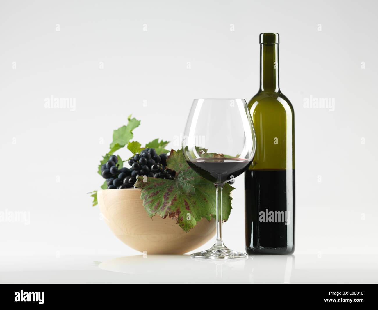 Bouteille de vin rouge, verre et bol de raisins sur fond blanc Banque D'Images