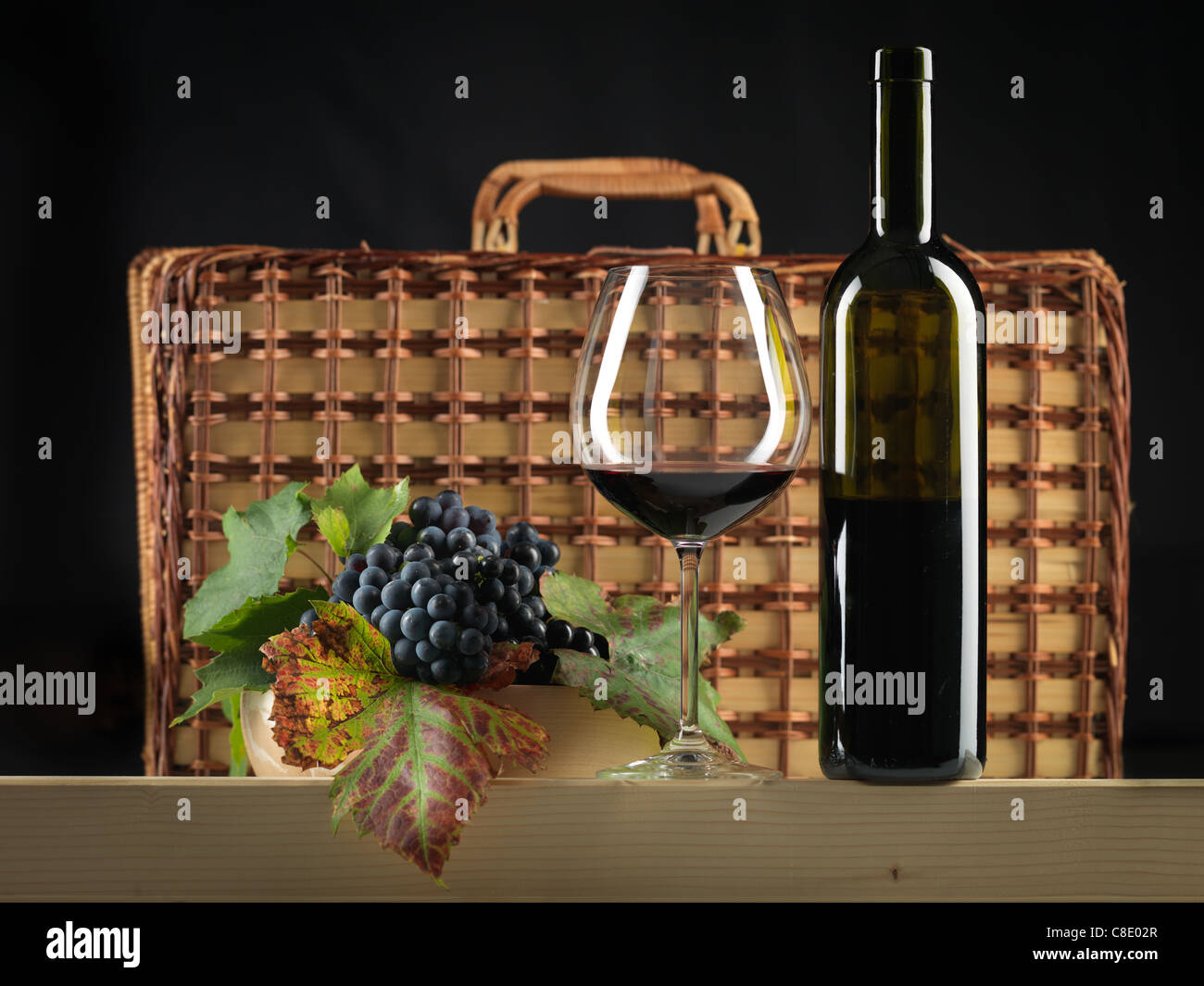 Bouteille de vin rouge, verre, raisins et panier pique-nique sur fond noir Banque D'Images
