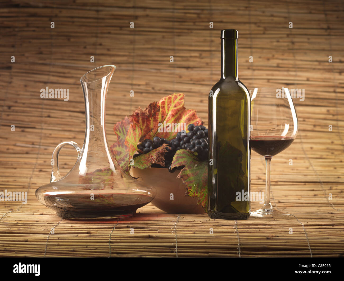 Bouteille de vin rouge, verre, pitcher et raisins sur fond d'osier Banque D'Images
