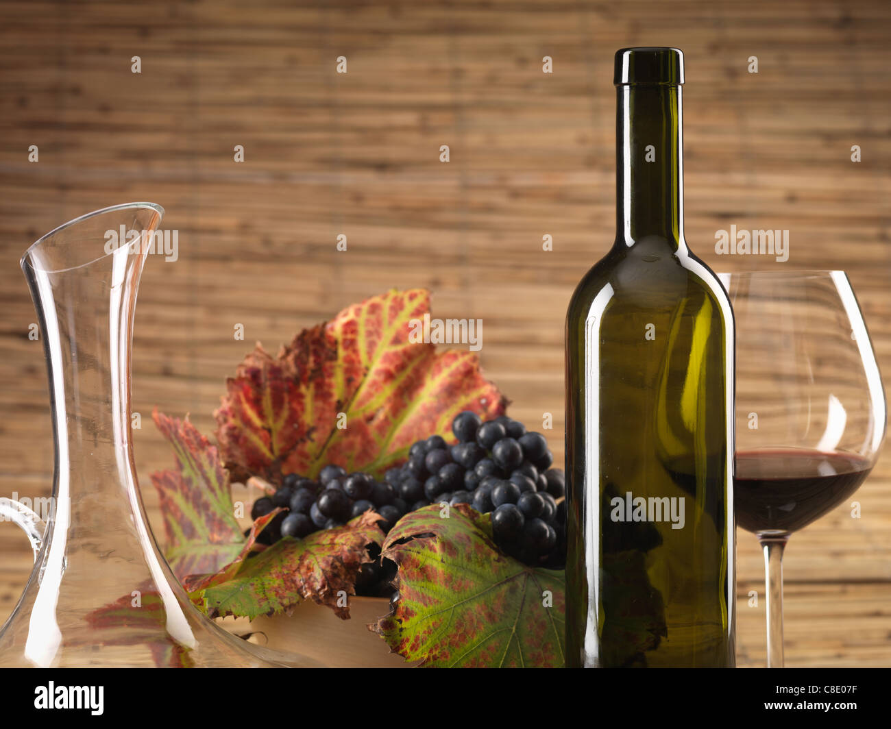 Bouteille de vin rouge, verre, pitcher et raisins sur fond d'osier Banque D'Images