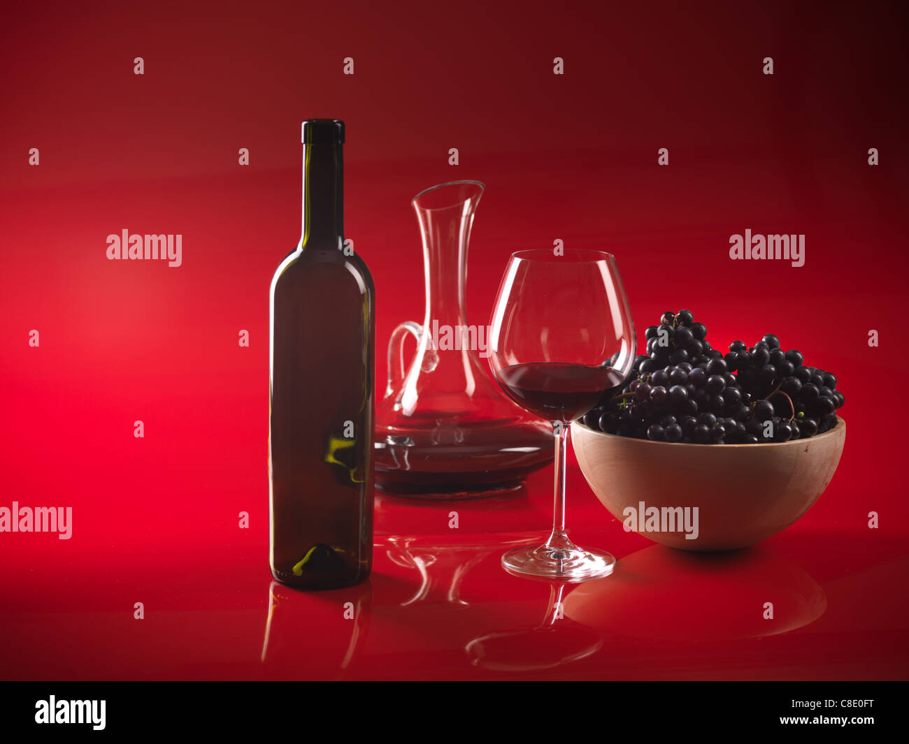 Verre de vin rouge, bouteille, bol avec les raisins et carafe sur fond rouge Banque D'Images