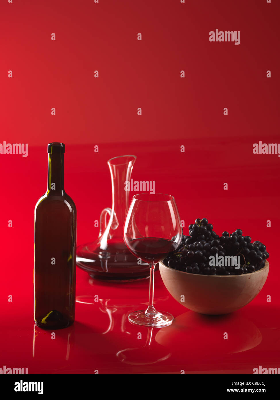 Verre de vin rouge, bouteille, bol avec les raisins et carafe sur fond rouge Banque D'Images