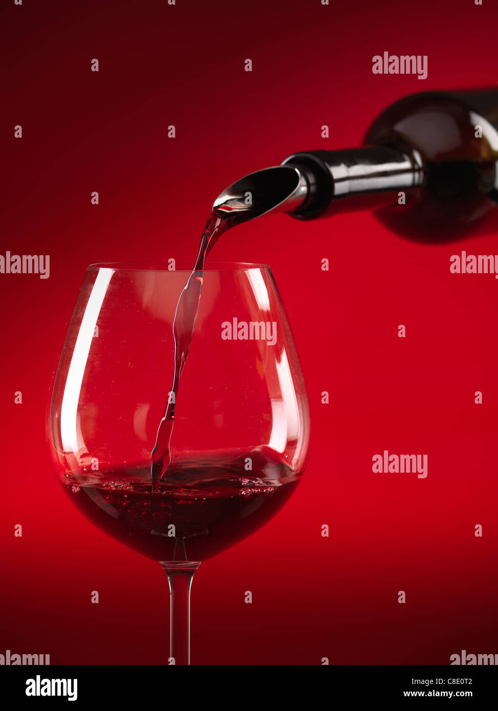 Détail de vin rouge est versé dans le verre sur fond rouge Banque D'Images