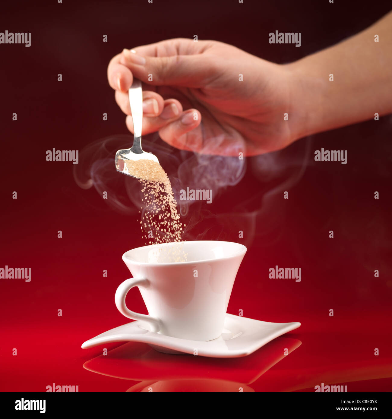 Woman's hand pouring sucre brun en tasse de café blanc sur fond rouge Banque D'Images