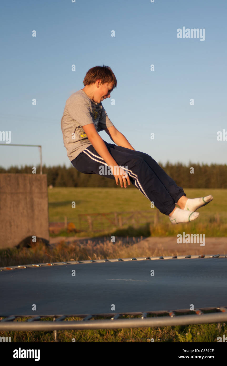 Teenage boy sur un trampoline sur un jour d'été en juillet, qui rebondit  dans l'air en position assise Photo Stock - Alamy