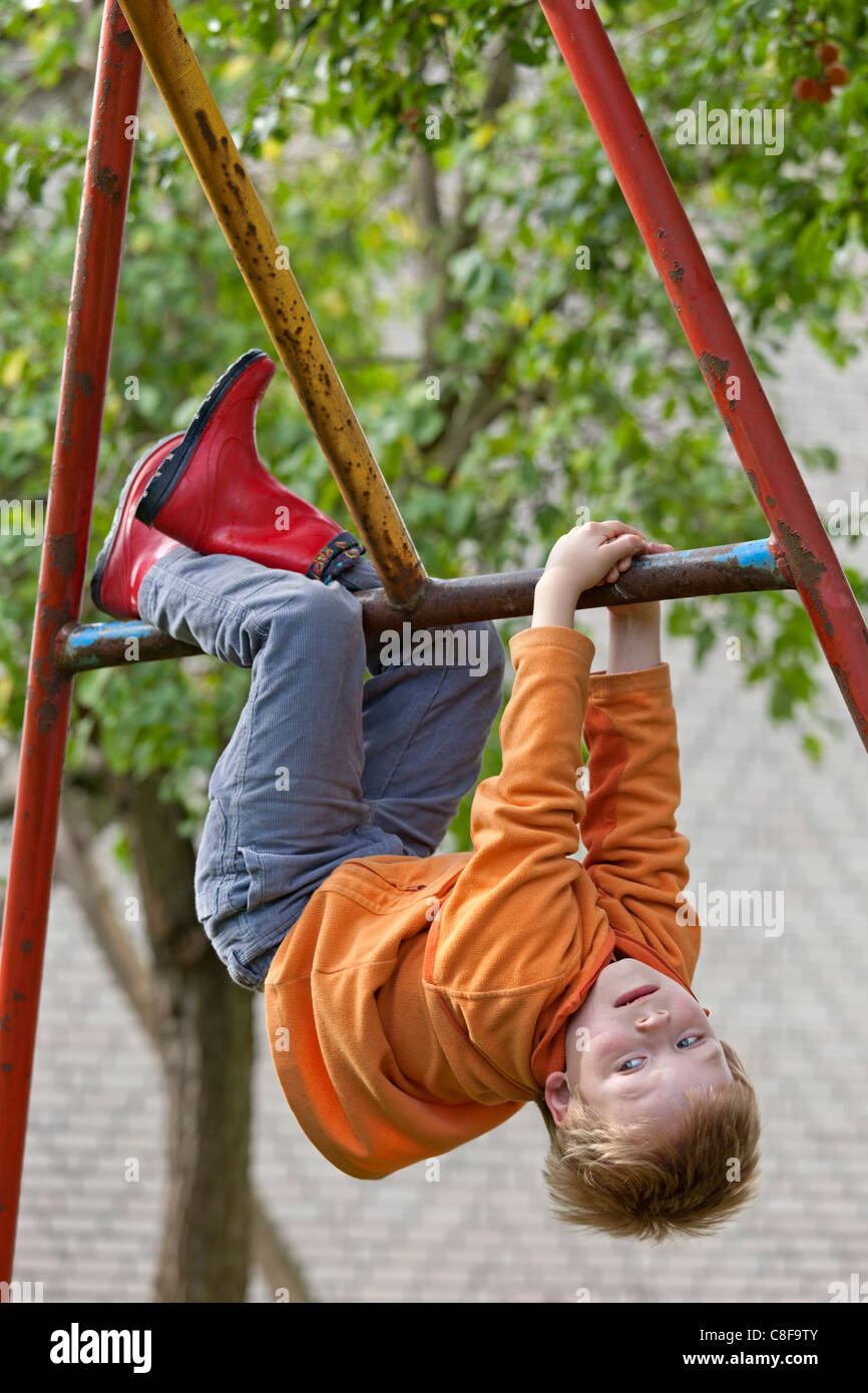 Jeune garçon hanging off monkey bars Banque D'Images