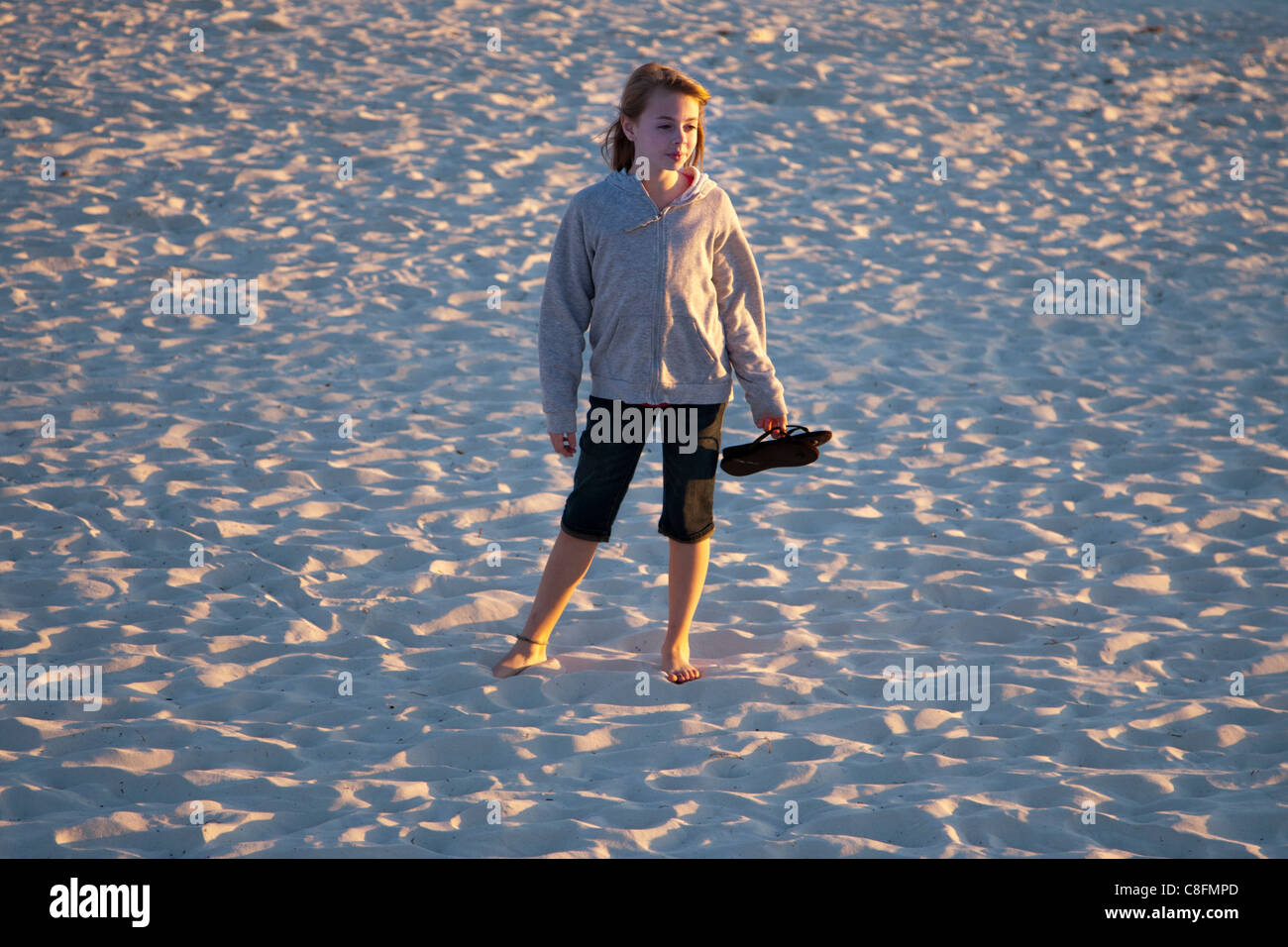 Jeune fille tenant une paire de sandales comme elle se tient dans le sable Banque D'Images