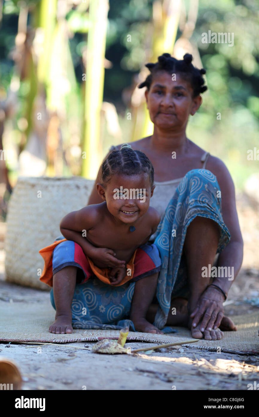 Une jeune fille et sa grand-mère avec des coiffures traditionnelles en dehors de leur hutte à Nosy Sakatia, près de Nosy Be (Nossi-bé), Madagascar Banque D'Images