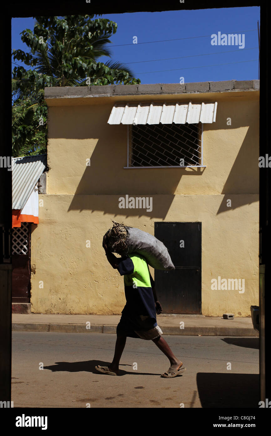 Un homme portant un sac de feuilles sur son épaule promenades par un café porte avant dans Be Hell-Ville, Nosy Be, Madagascar Banque D'Images