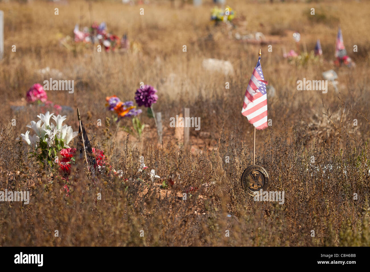 Cimetière négligé, envahie par les mauvaises herbes avec drapeau à vent, des fleurs en plastique et des roches et des pierres autour de monticule de terre tombe. Banque D'Images