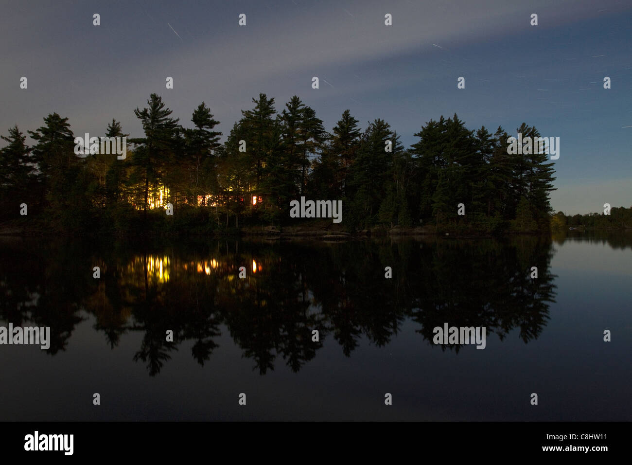 Star Trail dans ciel nuageux avec réflexion sur le lac avec feux cottage Banque D'Images