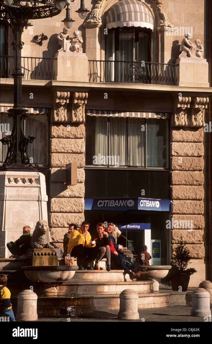 Budapest, Hongrie. Personnes (couple) assis sur les marches d'une fontaine de manger les aliments de McDonald's ; Citibank cash machine derrière. Banque D'Images