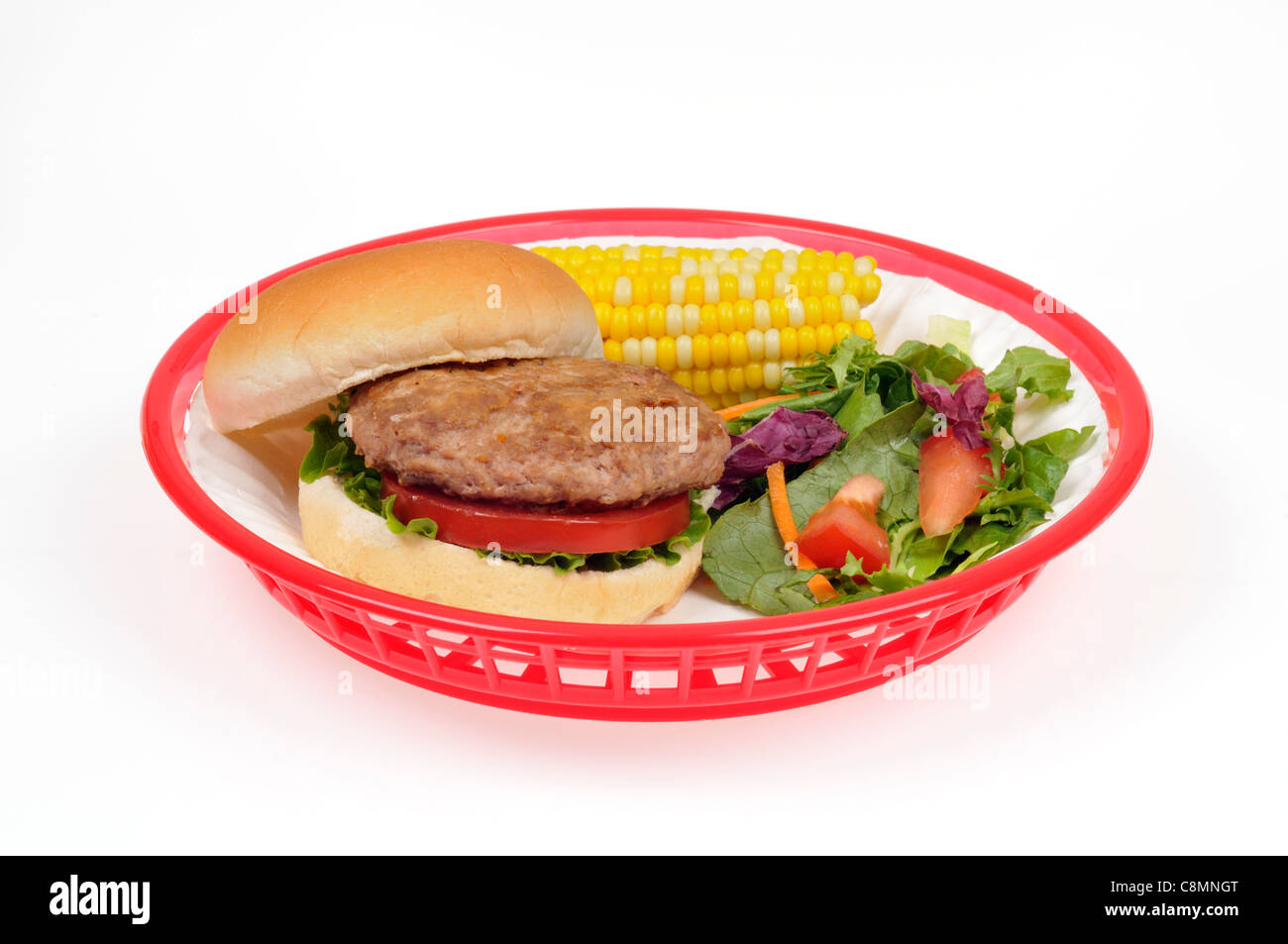 Hamburger de dinde avec de la laitue et la tomate en pain en plastique rétro rouge panier avec épi de maïs et salade verte sur fond blanc. Banque D'Images