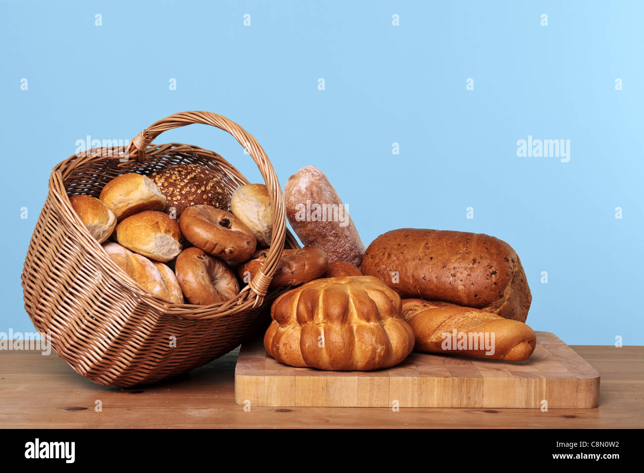 Photo de différents types de pains et de petits pains dans un panier en osier sur une table en bois avec fond bleu. Banque D'Images