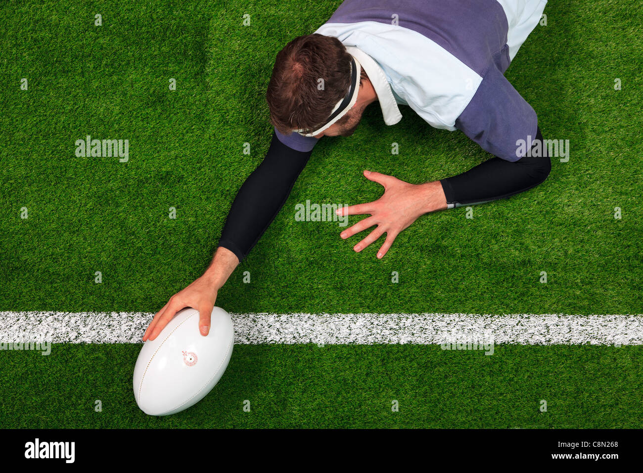 Photo prise à la verticale d'un joueur de rugby qui s'étend sur la ligne pour marquer un essai d'une main sur la balle. Banque D'Images