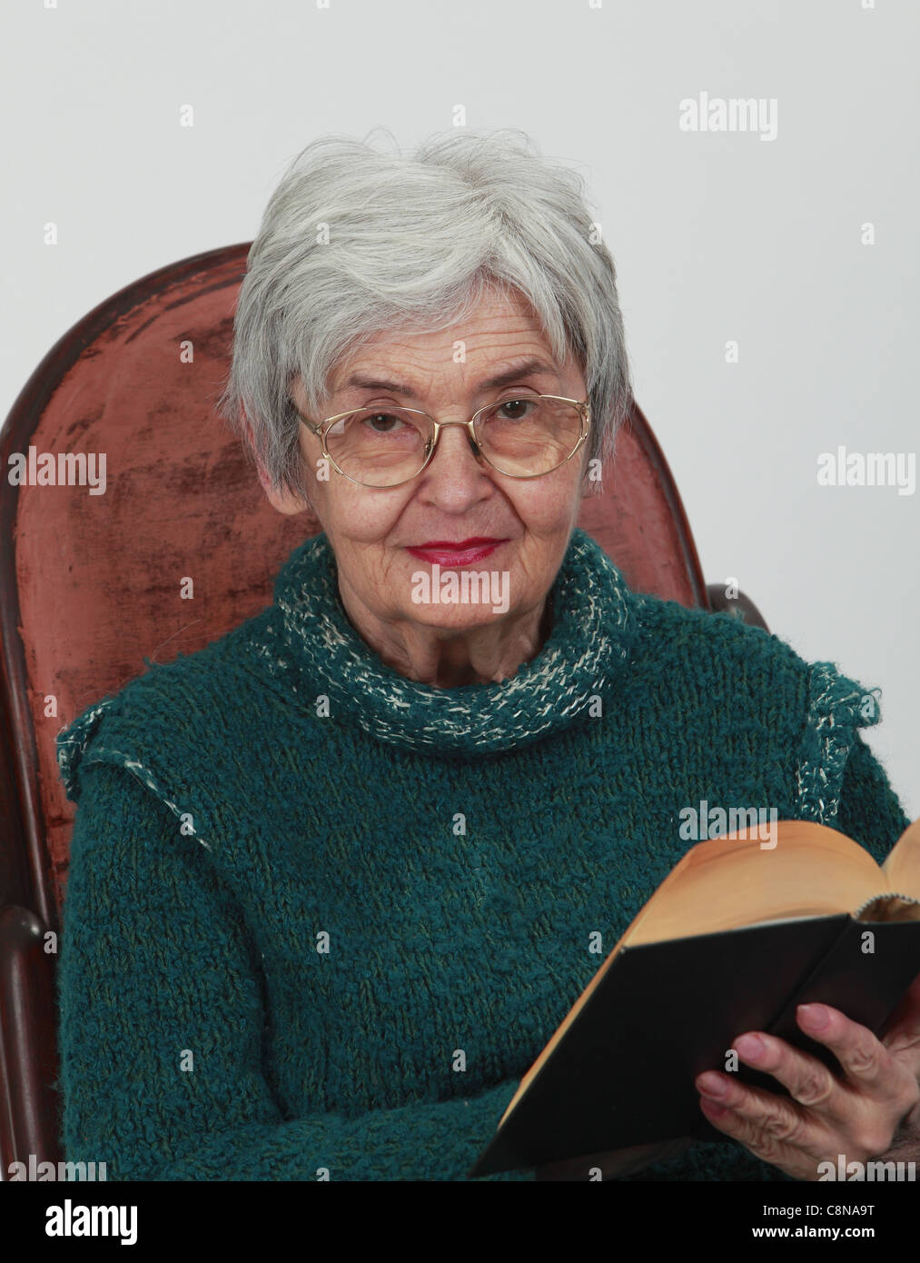 Portrait d'une vieille femme avec un livre noir sur fond gris. Banque D'Images