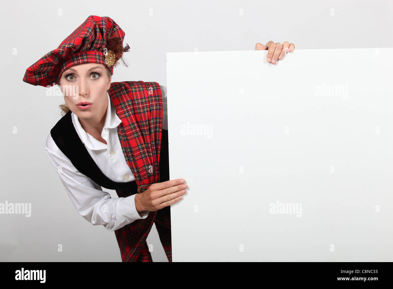 Surpris femme en costume traditionnel écossais avec un conseil laissée en blanc pour votre message Banque D'Images