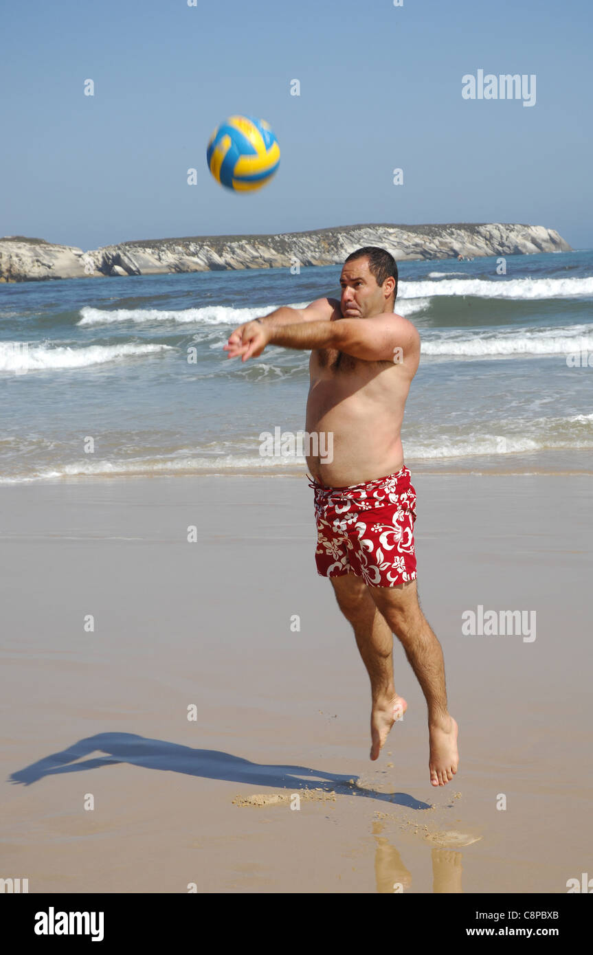 Gros homme jouant avec une balle sur la plage Banque D'Images