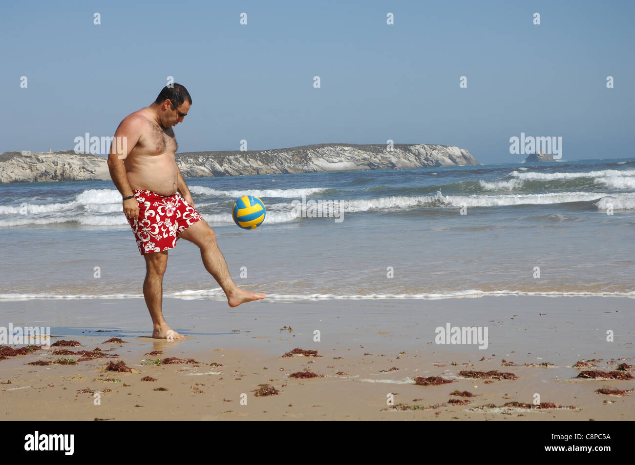 Gros homme jouant avec une balle sur la plage Banque D'Images