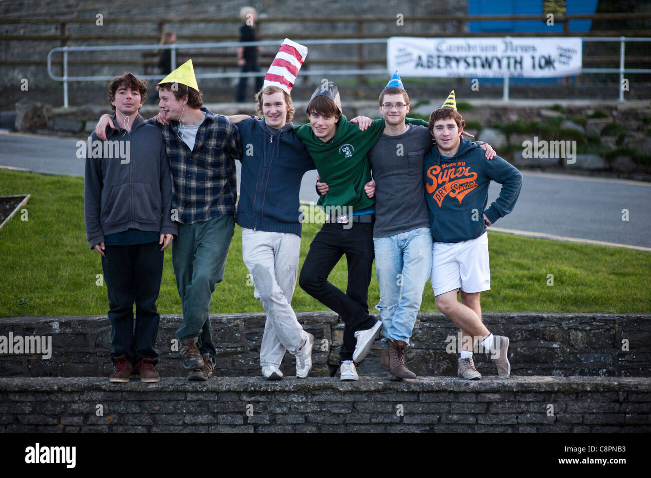 6 six étudiants de l'université de jeunes hommes portant des chapeaux de papier drôle, Aberystwyth, au crépuscule, en octobre 2011 Banque D'Images